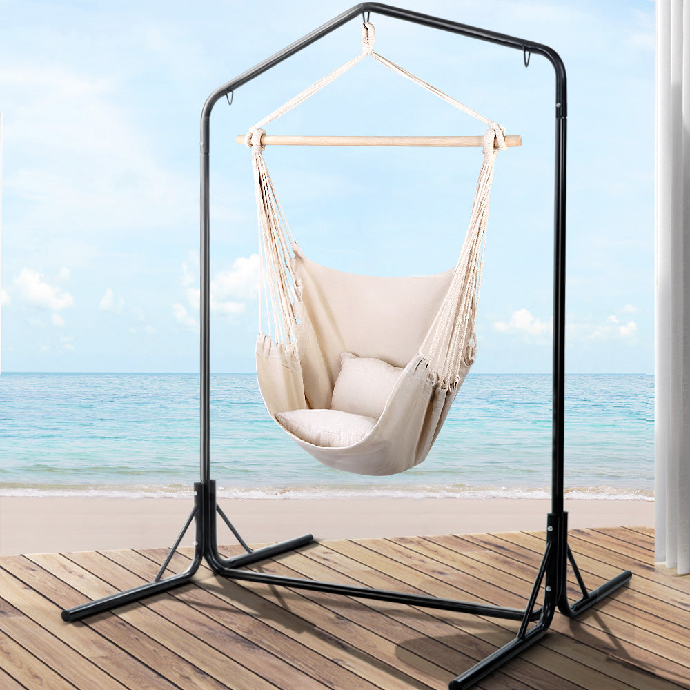 Cream hanging chair with its black steel stand in a seaside deck setting.