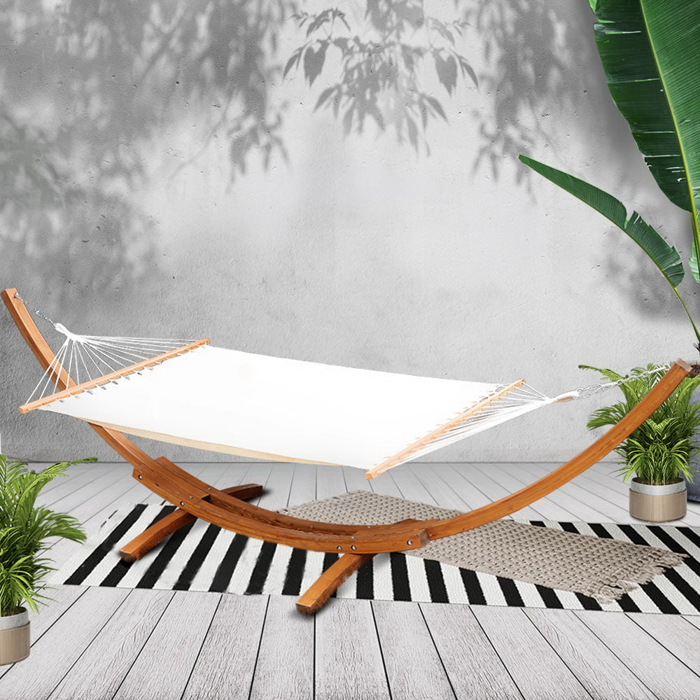 Cream hammock and curved timber stand on a deck with plants and a striped rug; styling accessories not included.