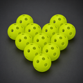 Twelve fluorescent green 26-hole indoor pickleballs on a charcoal studio background